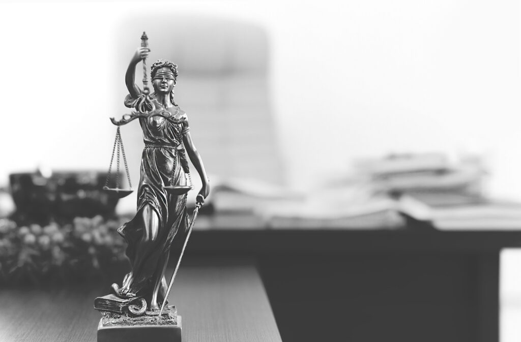 Picture of small statue of Lady Justice with desk in the background.